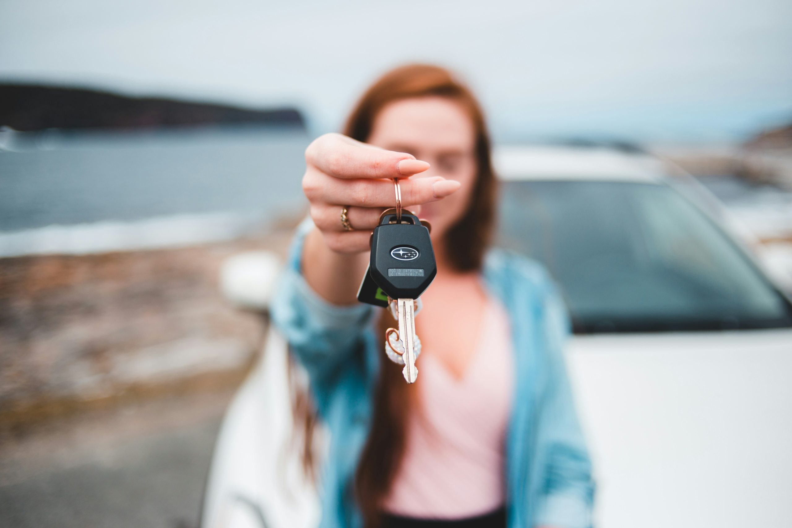 car key dangling from a woman's finger, with a white car in the background